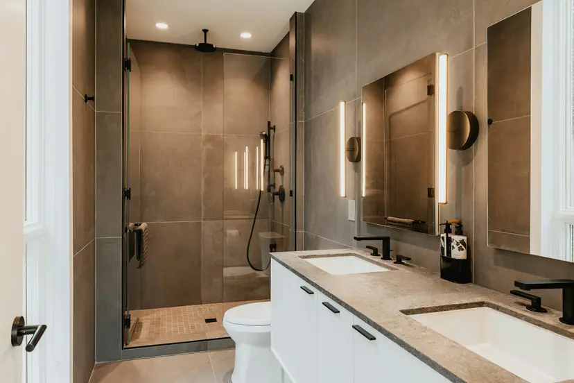 Yenilenmiş banyo; koyu tonlu büyük seramikler, cam panelli duş alanı ve beyaz lavabo dolabı